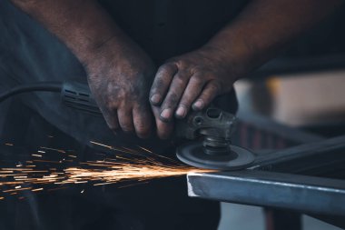 Profesyonel kumaş işçisi, endüstriyel atölyedeki elektrikli öğütücüyle çalışma masasında metal profili kesiyor..