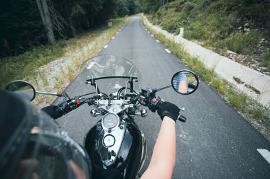 Close-up on the hands of a motorcycle driver riding on forest road. Travel and sport, speed and freedom concept