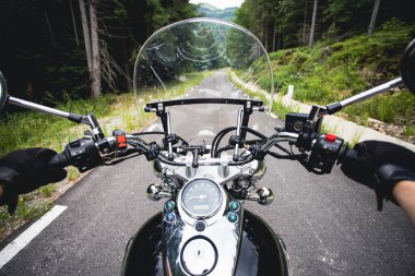 Orman yolunda giden motosikletli bir sürücünün ellerinde. Seyahat ve spor, hız ve özgürlük kavramı