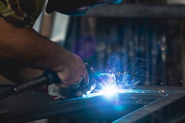 Etrafındaki kıvılcımlar uçuşurken tamirci atölyesinde kaynak ve öğütme yapıyordu. Koruyucu kask ve ekipman takıyor..