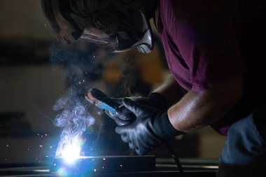 Etrafındaki kıvılcımlar uçuşurken tamirci atölyesinde kaynak ve öğütme yapıyordu. Koruyucu kask ve ekipman takıyor..