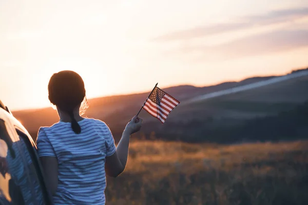Woman holding an American flag on a road trip. Independence Day or traveling in America concept.