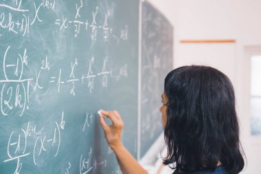 Okulda matematik dersi sırasında tahtaya yazı yazan öğretmen ya da öğrenci..