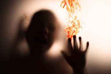 Horror ghost girl with blood on her hand behind the matte glass. Halloween festival concept.