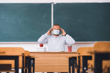 Sınıfta maskeli bir öğretmen var. Coronavirus salgını sırasında sosyal uzaklık ve sınıf güvenliği