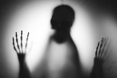 Horror skeleton or grim reaper behind the matte glass. Halloween festival concept.Blurred picture