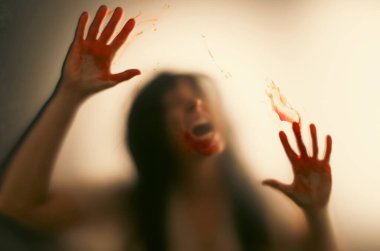 Horror ghost woman with blooded hands behind the matte glass. Halloween festival concept.