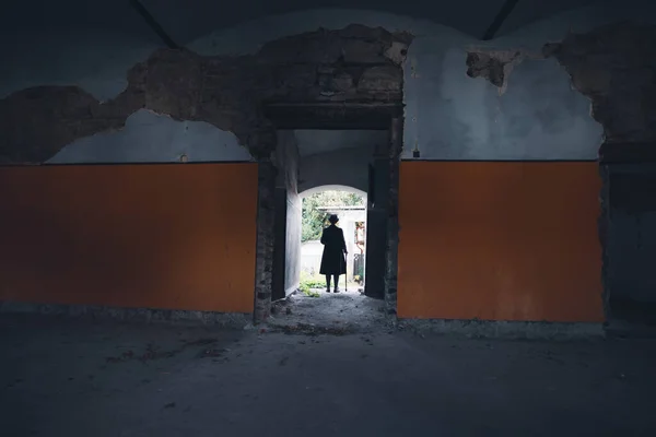 A mysterious figure wearing a long coat and fedora standing in a ruined, abandoned house