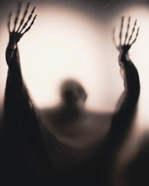 Horror skeleton or grim reaper behind the matte glass. Halloween festival concept.Blurred picture