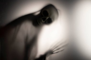 Horror skeleton or grim reaper behind the matte glass. Halloween festival concept.Blurred picture