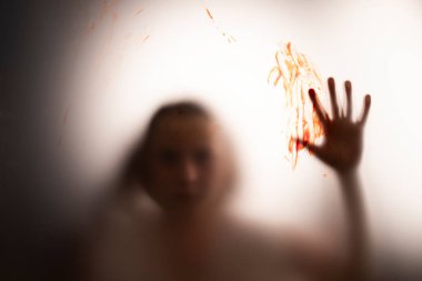 Horror ghost girl with blood on her hand behind the matte glass. Halloween festival concept.