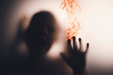 Horror ghost girl with blood on her hand behind the matte glass. Halloween festival concept.