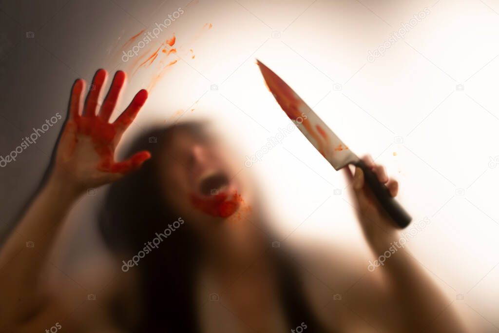 Horror, halloween background - Shadowy figure behind glass holding a knife and with blooded hands