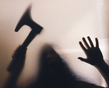 Korku, cadılar bayramı arkaplanı, camın arkasında elinde balta tutan karanlık bir figür.