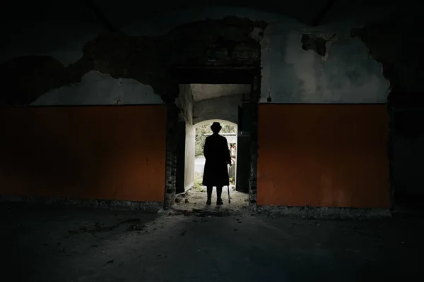 A mysterious figure wearing a long coat and fedora standing in a ruined, abandoned house