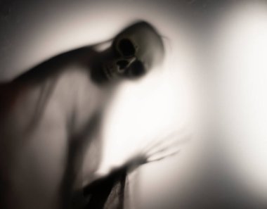 Horror skeleton or grim reaper behind the matte glass. Halloween festival concept.Blurred picture