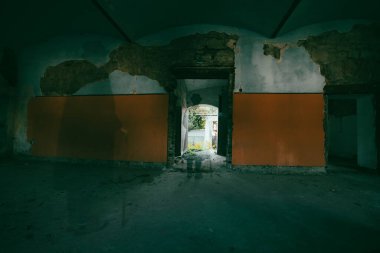 A mysterious figure wearing a long coat and fedora standing in a ruined, abandoned house