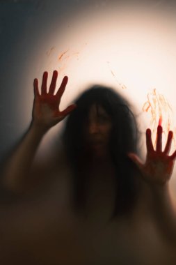 Horror ghost woman with blooded hands behind the matte glass. Halloween festival concept.