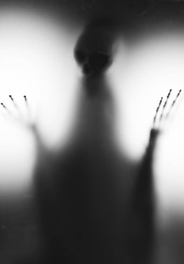 Horror skeleton or grim reaper behind the matte glass. Halloween festival concept.Blurred picture