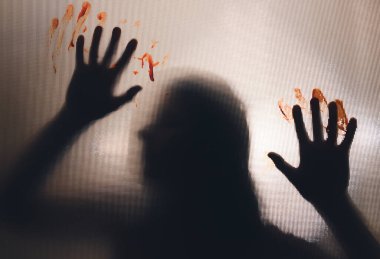 Horror ghost woman with blooded hands behind the matte glass. Halloween festival concept.