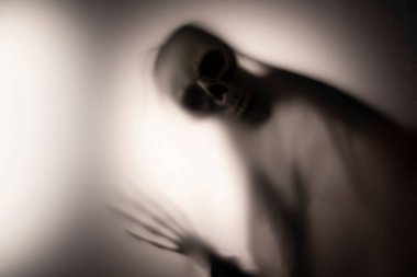Horror skeleton or grim reaper behind the matte glass. Halloween festival concept.Blurred picture