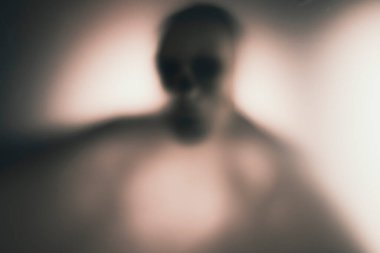 Horror skeleton or grim reaper behind the matte glass. Halloween festival concept.Blurred picture