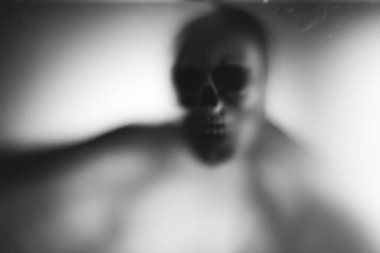Horror skeleton or grim reaper behind the matte glass. Halloween festival concept.Blurred picture
