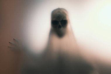 Horror skeleton or grim reaper behind the matte glass. Halloween festival concept.Blurred picture