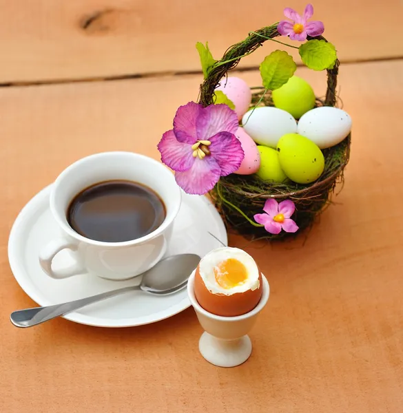 Colorful painted easter eggs in basket, a cup of black coffee and egg cup — Stock Photo, Image