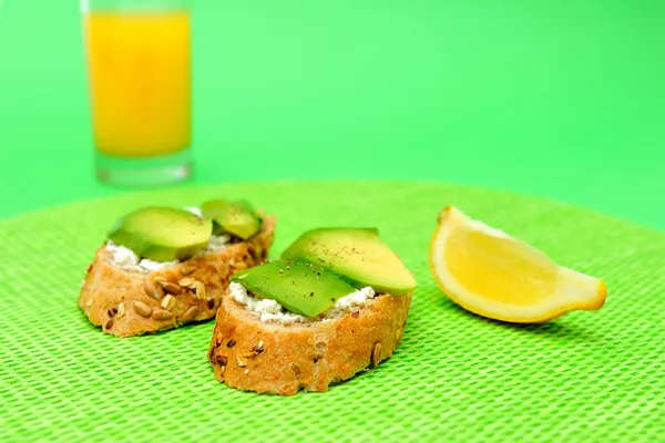 Gesunde Avocado-Snacks und ein Glas Orangensaft auf grünem Hintergrund Stockbild