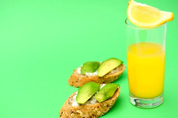 Gesunde Avocado-Snacks und ein Glas Orangensaft auf grünem Hintergrund lizenzfreie Stockbilder
