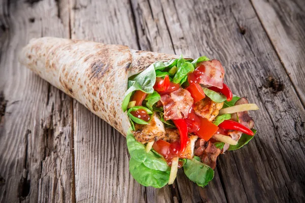 Kip segmenten in een tortilla wrap op hout. — Stockfoto