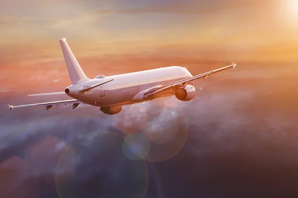 Avião comercial de passageiros voando acima das nuvens sob a luz do pôr do sol. — Fotografia de Stock