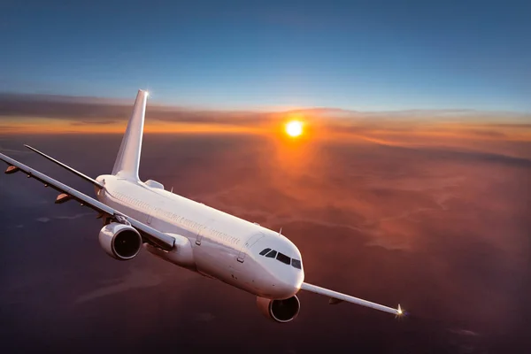 日没の光の中で雲の上を飛ぶ旅客商業航空機. — ストック写真