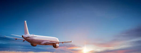 Avião comercial de passageiros voando acima das nuvens sob a luz do pôr do sol. — Fotografia de Stock