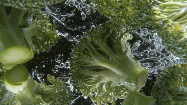 Spadanie świeżych brokułów do wody, czarne tło. — Zdjęcie stockowe