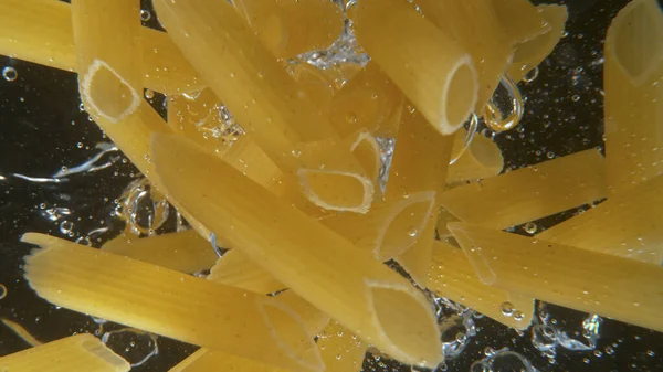 Caída de pasta italiana sin cocer Penne en el agua. —  Fotos de Stock