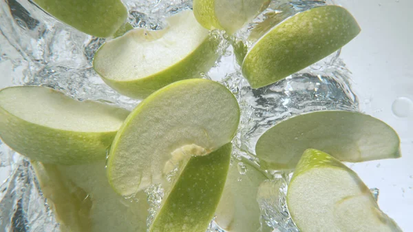 Piezas frescas de manzanas cayendo en el agua, congelar el movimiento. —  Fotos de Stock