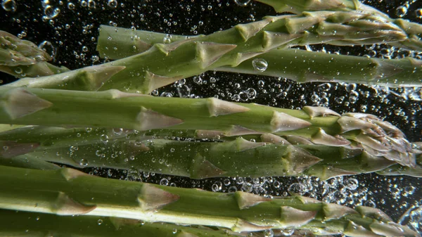 Falling fresh asparagus into water, black background. — Stock Photo, Image