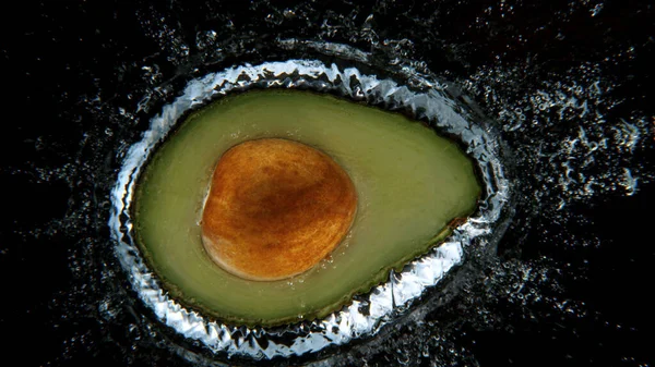 Falling fresh avocado into water, black background. — Stock Photo, Image