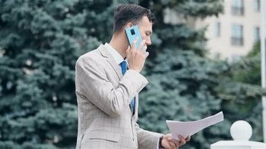 Akıllı telefondan konuşan ve iş raporlarını elinde tutan bir tüccar. İş ve Bilgi Teknolojisi Konsepti.