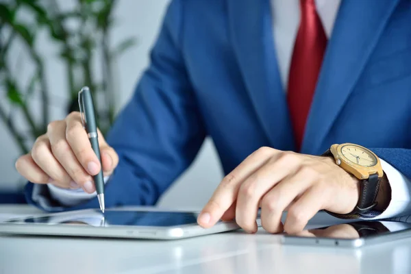 Trader man with pen in hand checks business report on digital tablet screen. Business and financial analysis concept. Close up