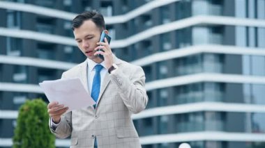 Borsa simsarı akıllı telefondan konuşuyor ve iş raporlarını elinde tutuyor. İş ve Bilgi Teknolojisi Konsepti.