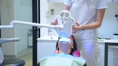 Diş hekimi klinikte dişleri beyazlatan lazer uygulaması uyguluyor. Hasta için diş beyazlatma. Yavaş Hareket Efekti.