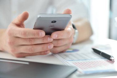 Yönetici ofisinde oturuyor ve akıllı telefondan mesaj yazıyor. İş ve iş kavramı. Kapat.