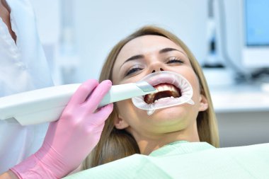 Kadın dişçi, diş sağlığı kliniğinde diş taraması yaparken diş içi tarayıcı kullanıyor. Modern tarama makinesi konseptiyle dahili tarama.
