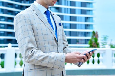 Takım elbiseli genç işadamı akıllı telefon kullanıyor. İş dünyası ve inşaat kavramı.