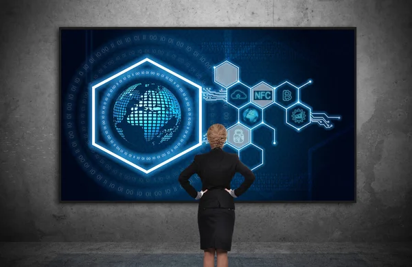 ハード画面上のデジタルビジネスアイコンと仮想六角形のホログラムを探しているビジネスマンの女性 コンクリート暗い部屋 仮想現実とグローバルネットワークの概念 — ストック写真