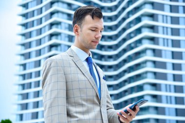 Elinde cep telefonu olan genç bir işadamı modern binanın yanında duruyor. İş ve teknoloji kavramı.