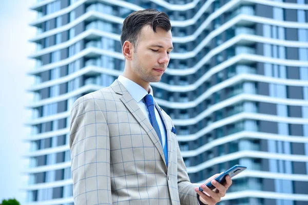 Elinde cep telefonu olan genç bir işadamı modern binanın yanında duruyor. İş ve teknoloji kavramı.